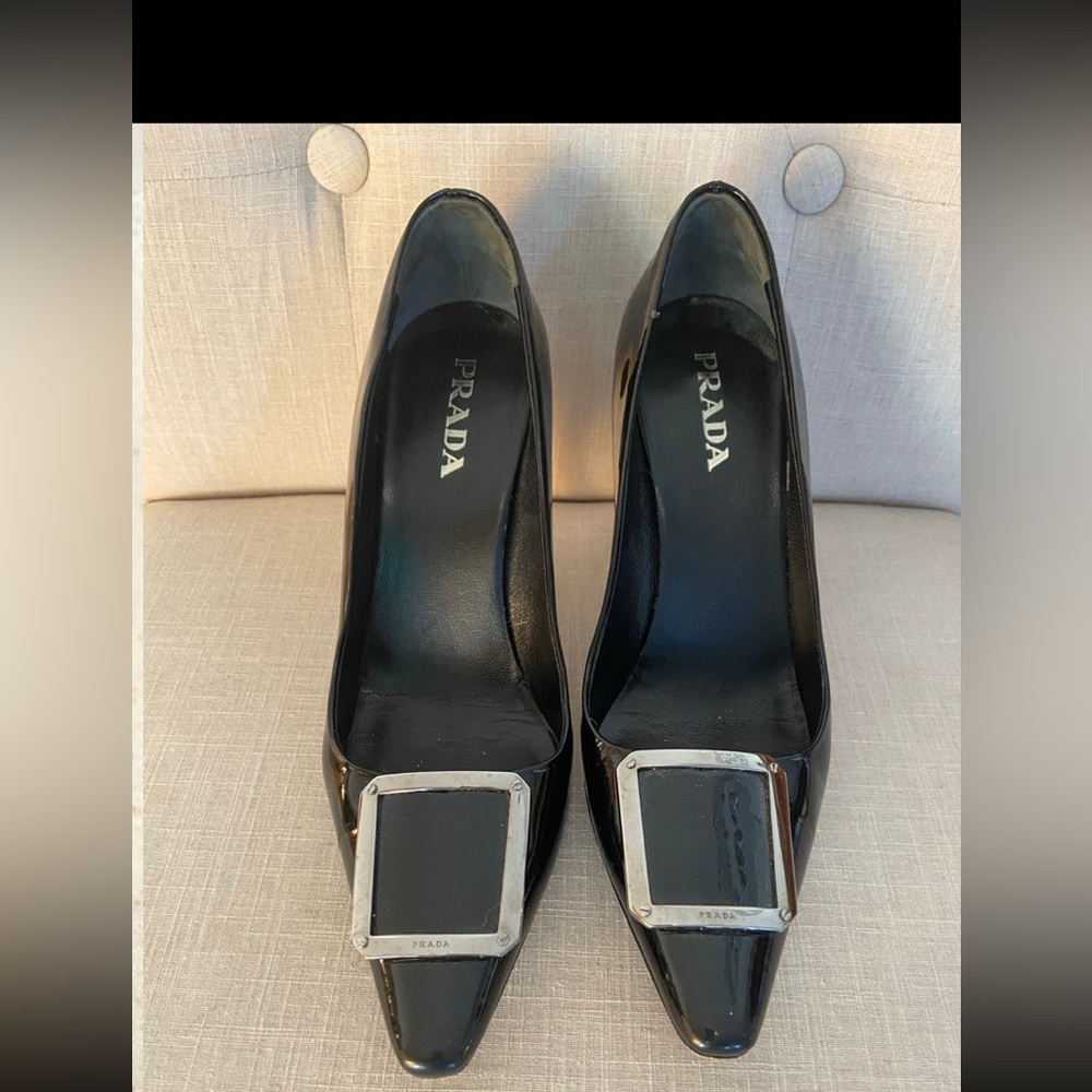 Prada black patent leather pump with large silver buckle.
